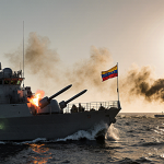 US naval vessel firing missiles at smoke‑filled boat with Venezuelan flag flying