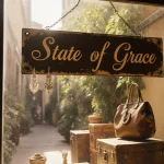 Vintage storefront with wooden sign reading State of Grace and antique jewelry displayed in golden sunlight