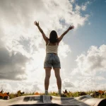 Summer person stretching arms upward with warm sunlight and scattered leaves on the ground