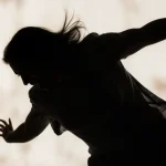Woman crashing down with arms outstretched, silhouette against harsh light and blurred doorway.